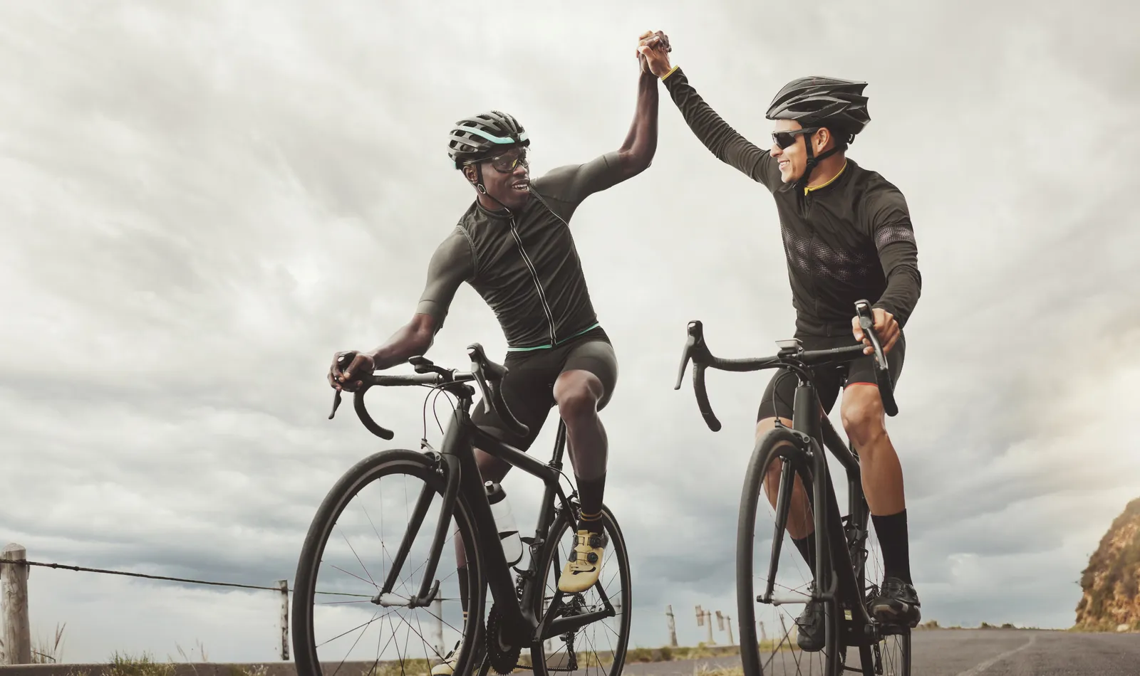 Two cyclists high-fiving at the top of a climb